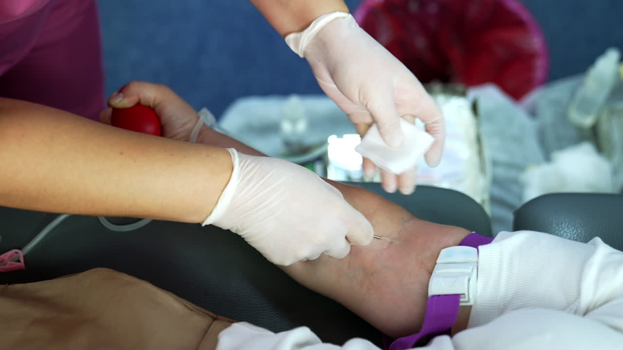 A thick needle is inserted into the donor's arm. The drip is attached to the hand for blood donation. Close up.