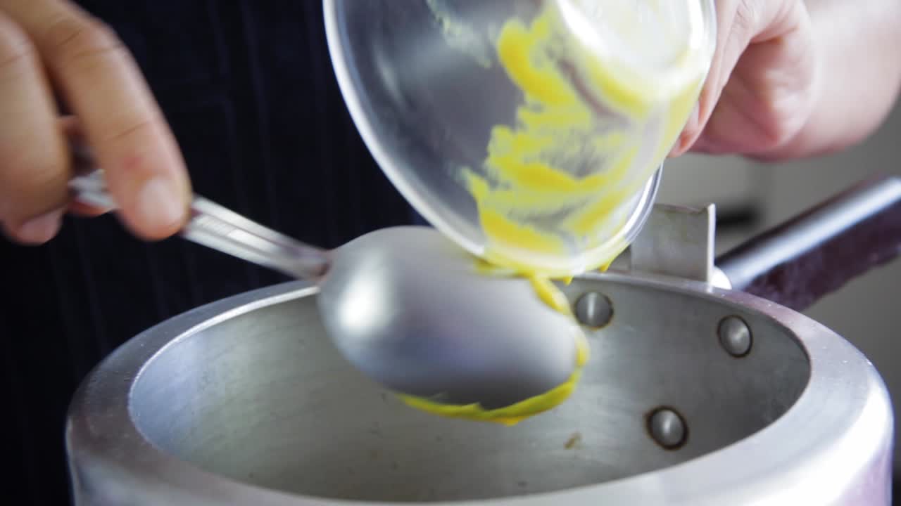 Manos de mujer añadiendo mostaza de un pequeño cuenco transparente con una cuchara dentro de una olla a presión