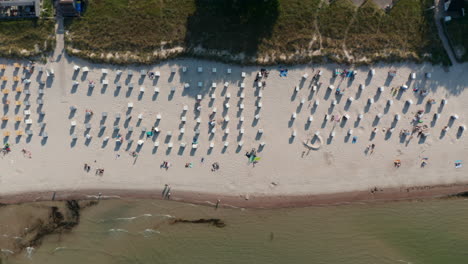 Ojo-De-Pájaro-Aéreo-Vista-De-Arriba-Hacia-Abajo-De-La-Playa-Turística-En-Scharbeutz,-Alemania,-Con-Sillas-De-Playa-Y-Gente-Tomando-El-Sol,-De-Lado,-Día-Soleado