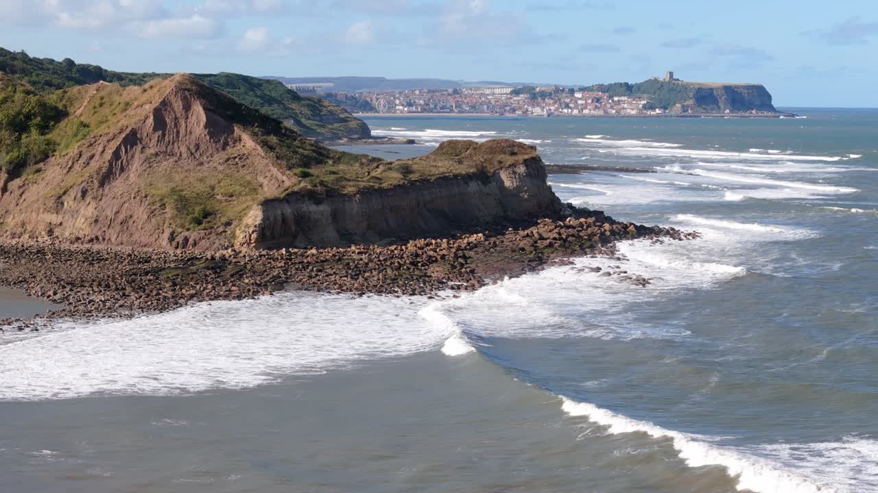 aerial drone footage of Scarborough taken from a distance away over Cayton Bay with blue sky and ocean and big waves