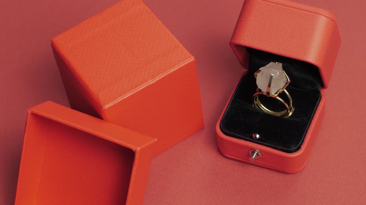 Pan shot of a gold ring with a raw gemstone in a luxurious velvet jewelry box, surrounded by open packaging on a stylish background