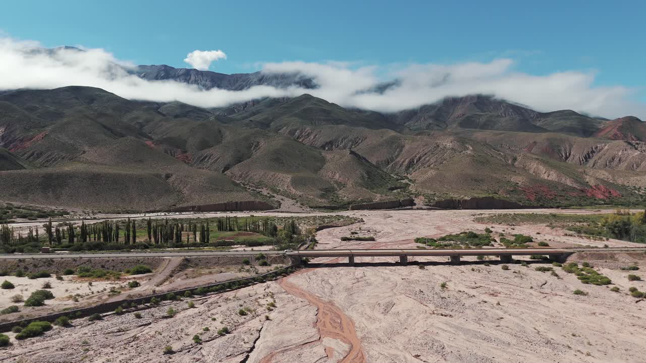 마른 강을 가로지르는 다리에서 차가 운전하는 느린  촬영, 배경에는 구름이 가득한 산, 아르헨티나의 주주이 지방