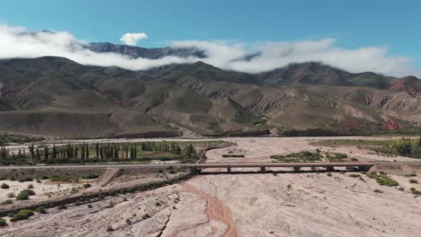 pan lento disparado en el puente sobre el río seco con un coche conduciendo, montañas nubladas en el fondo, provincia de jujuy en argentina