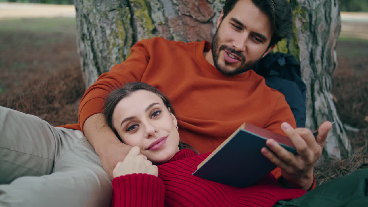 coppia di famiglie che leggono un libro al fine settimana del parco naturale insieme verticalmente da vicino.