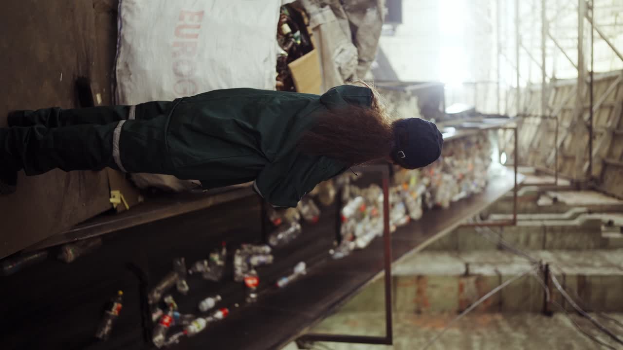 A young African-American woman checks a conveyor belt at a recycling plant. Pollution control. Zoom-out