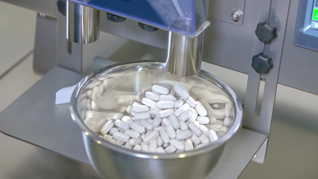 White pills for COVID-19 treatment falling into a tray at the pharmaceutical lab