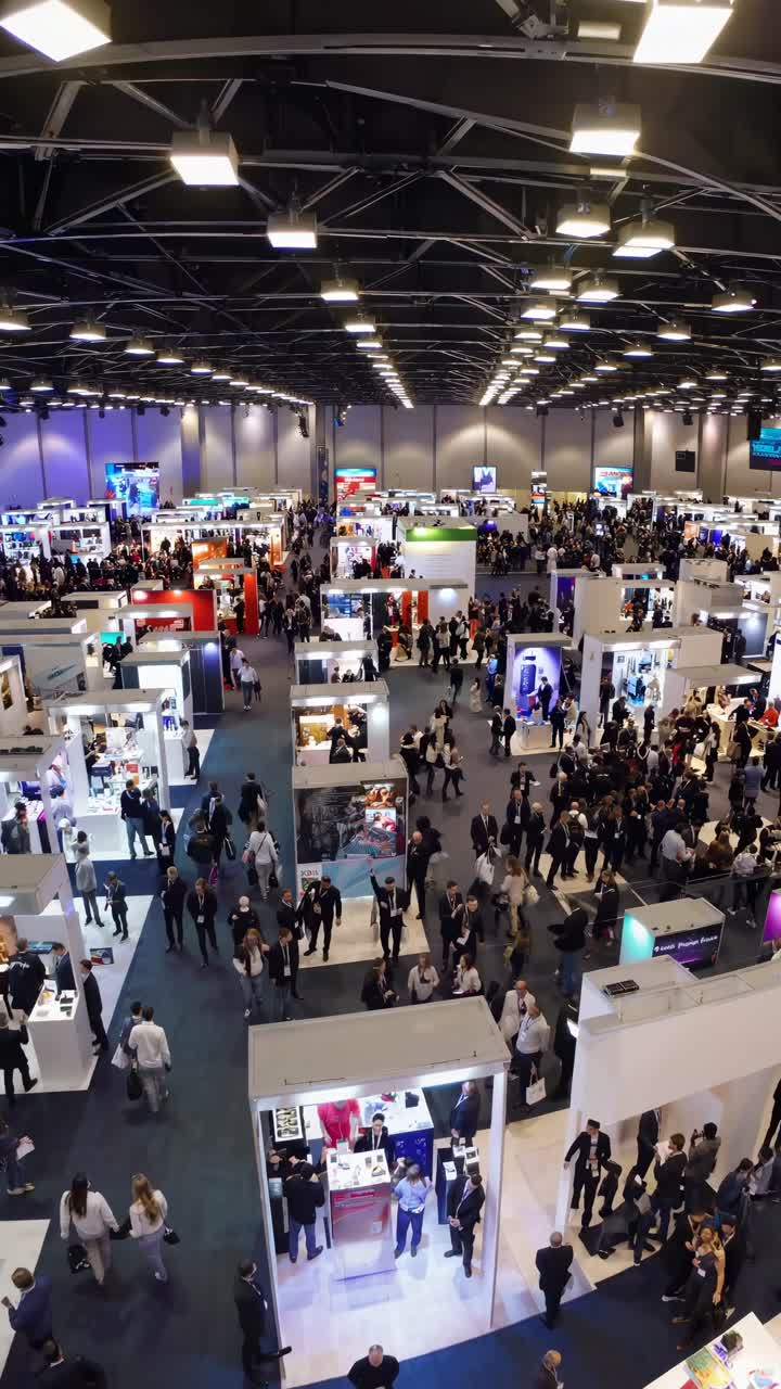 Inquadratura dall'alto di un'affollata fiera commerciale con numerosi stand e partecipanti, che cattura la dinamicità