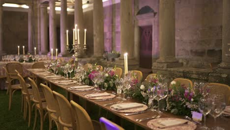 long wedding reception table with floral decor, glassware, and candelabras under purple lighting