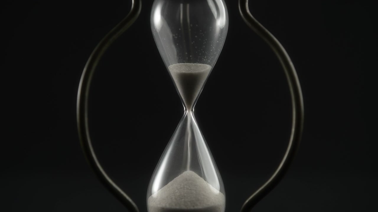 Sand Flowing Through a Vintage Hourglass on Black Background