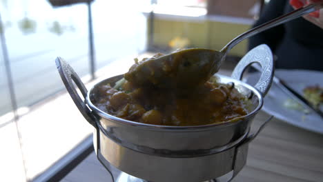 lifting a spoon out of hot indian food or curry dishes with steam