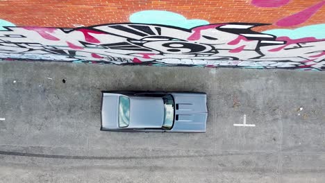 Aerial---bird's-eye-view-of-a-vintage-car-in-an-abandoned-warehouse-parking-lot