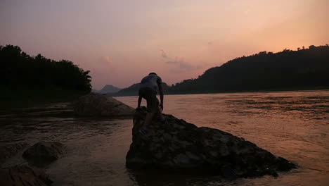 boy standing on a rock at sunset by the river