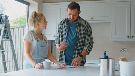 couple renovating kitchen at home looking at paint swatches on coffee break