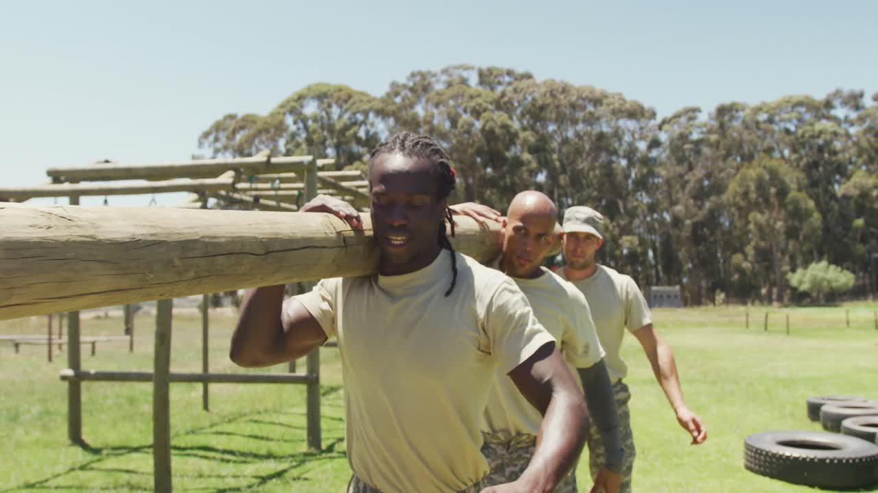 Diverse fit group of soldiers carrying tree log together in the sun at army obstacle course in field