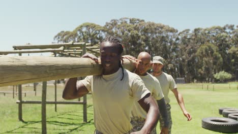 diverse fit group of soldiers carrying tree log together in the sun at army obstacle course in field