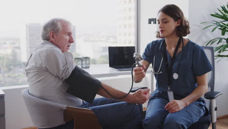 nurse wearing scrubs in hospital office checking senior male patients blood pressure