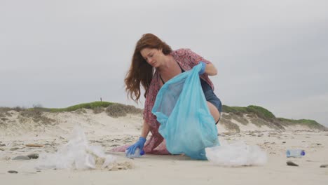 caucasian woman wearing latex gloves collecting rubbish from the beach looking ahead