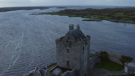 cámara aérea que captura el castillo de dunguaire en galway, revelando la belleza escénica de la bahía de kinvara y la ciudad durante el crepúsculo