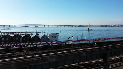 A-drone-shot-in-front-of-elevated-train-tracks-near-a-bay-in-Queens,-NY