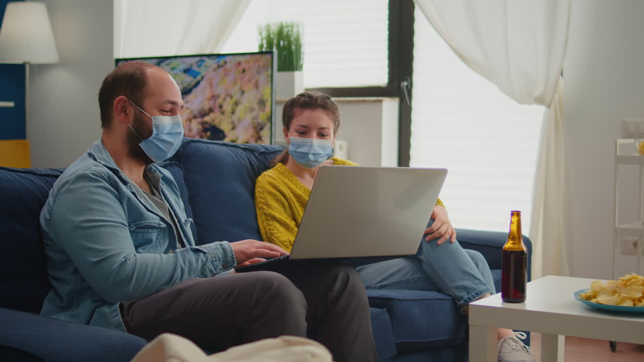 Friends looking at laptop socializing during party wearing protection mask