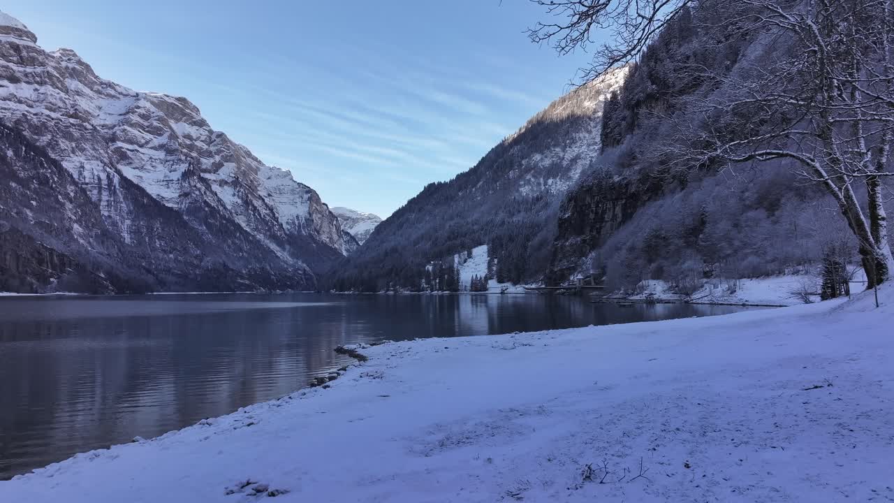 스위스 알프스 산맥의 전형적인 겨울날에 클론탈레르 호수의 눈 인 연안을 날아다니는 드론.