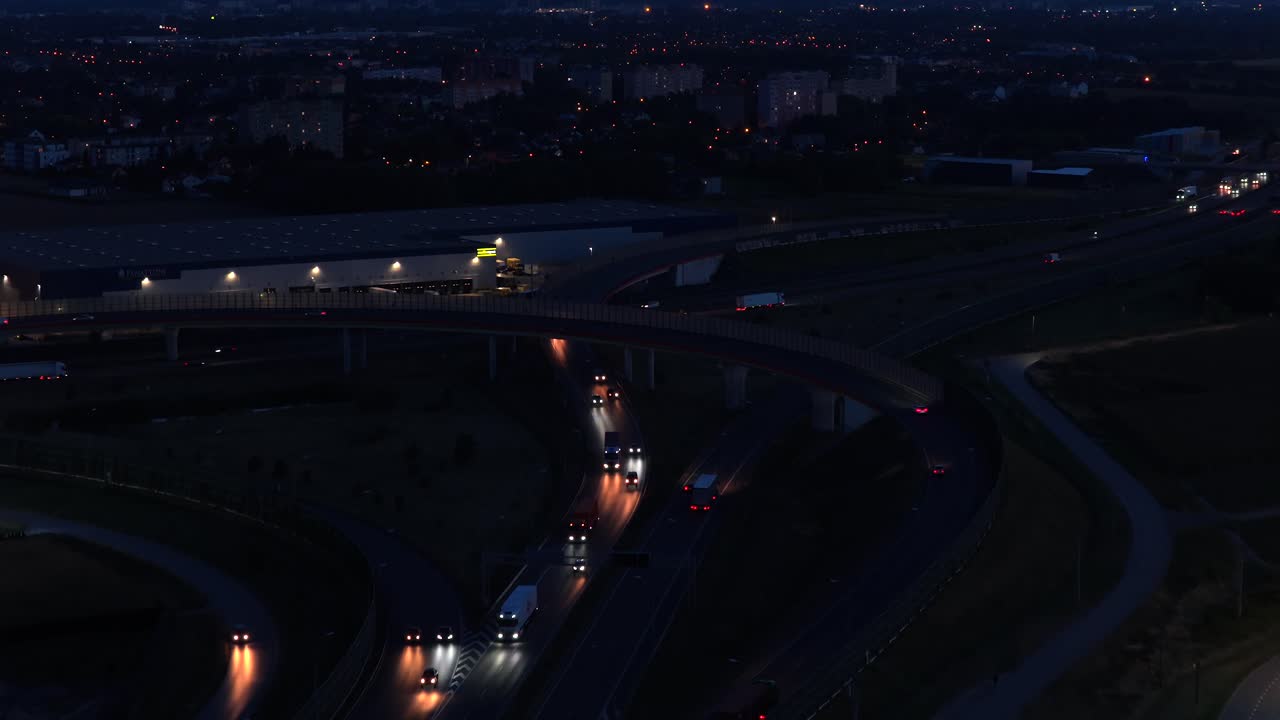 Aerial flyover multi level highway junction in Warsaw, Poland at night. Modern city with busy traffic scene and headlights of cars. Wide shot