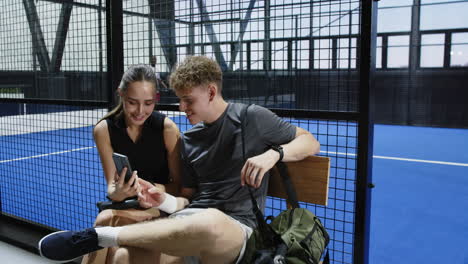 resting on bench, young athletes discussing padel tennis strategy after match, on indoor court