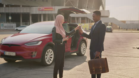 businesswoman and businessman exchanging keys for a new electric car at a parking lot.