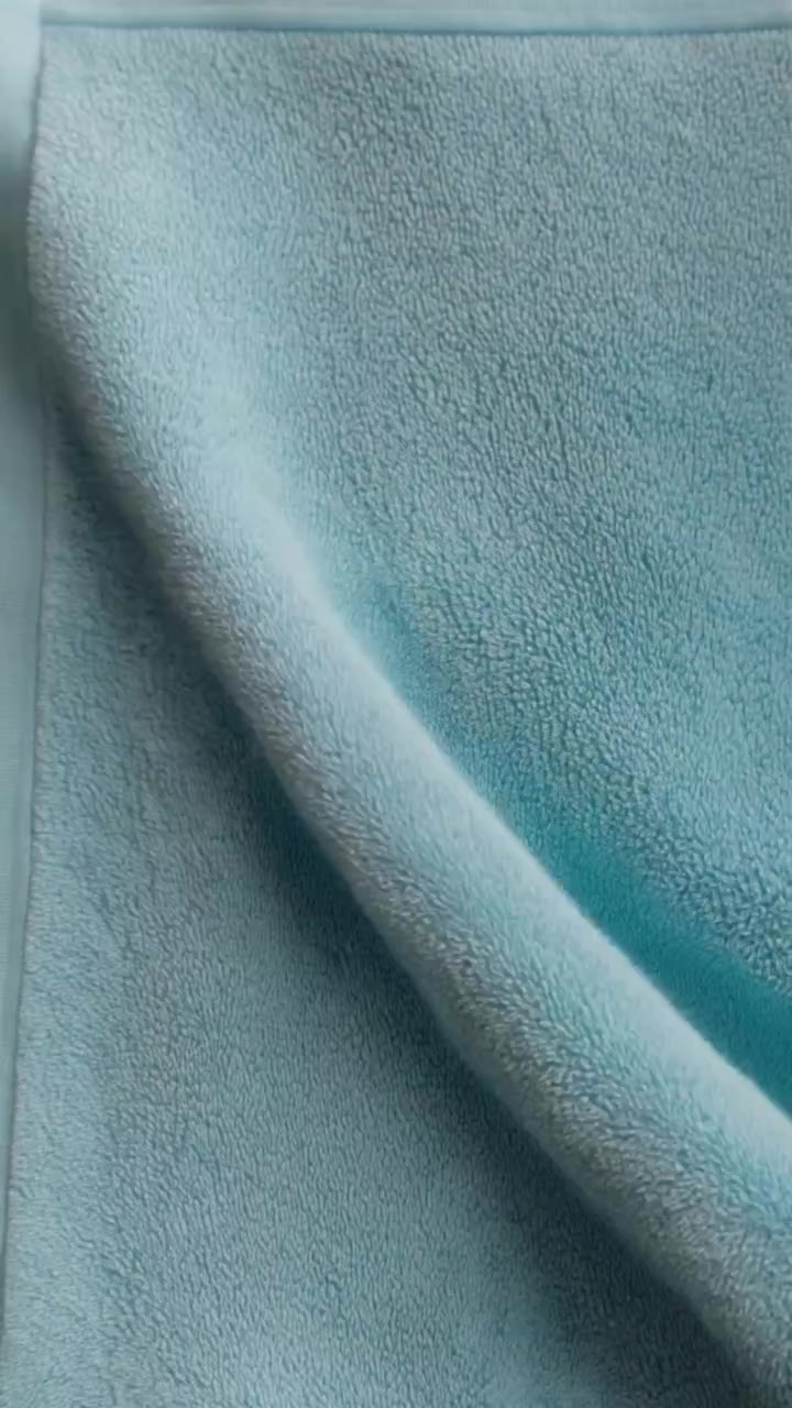 Um tecido de toalha azul ciano suave exibe dobras sutis e uma borda costurada em movimento suave