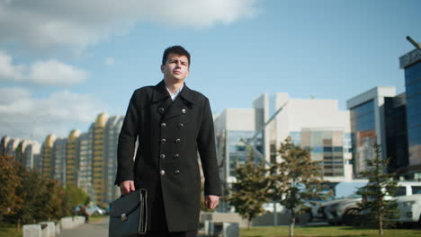 politician walking confidently outdoors holding briefcase, with leaves fluttering in wind, surrounded by modern glass buildings, urban trees, and vibrant environment under clear blue sky