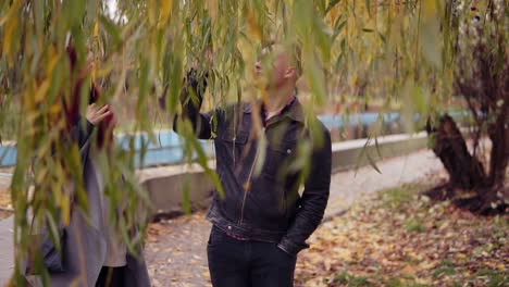 Romantisches-Junges-Paar,-Das-Tagsüber-Unter-Dem-Baum-Im-Herbstpark-Spaziert.-Die-Decke-Aus-Goldenen-Blättern-Auf-Dem-Boden.-Warmes-Wetter-Im-Herbst