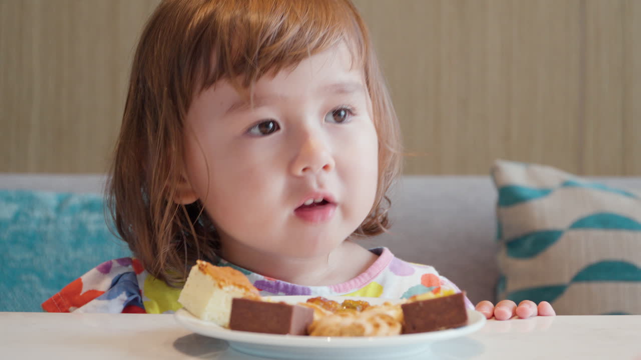 Toddler girl eats raisins and cakes - closeup