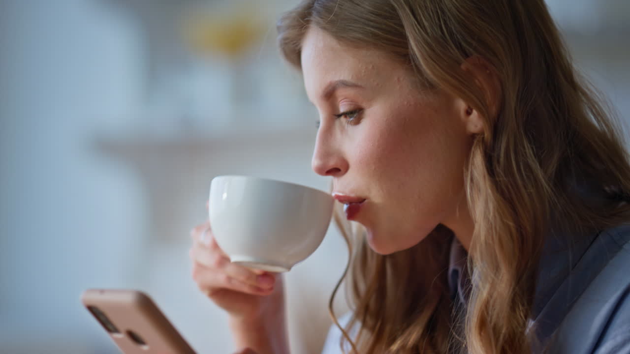 Girl hands holding cellphone enjoying morning coffee at windows kitchen closeup