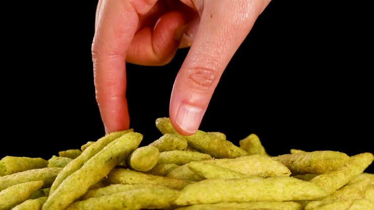 Human hand picks up green pea puffed snack, close-up, isolated on black background, studio lighting