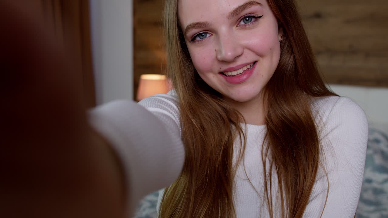 젊은 웃는 여성 블로거가 집에서 소셜 미디어 네트워크를 위해 스마트폰으로 셀피를 찍는 pov