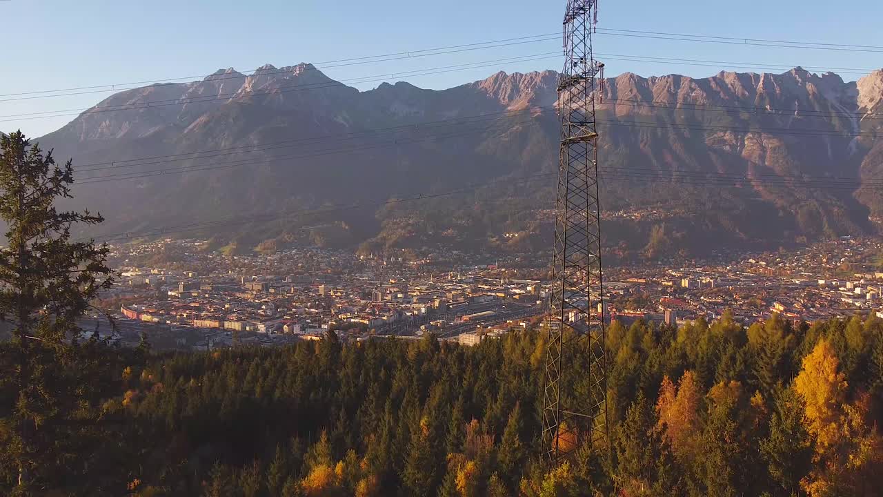 Areal drone overview of the city of Innsbruck with electricity mast in the foreground, mountains in the background at sunset