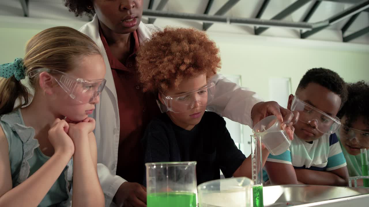Female teacher teaching youth in lab, pointing, steadying as curly youth pouring cup into cylinder