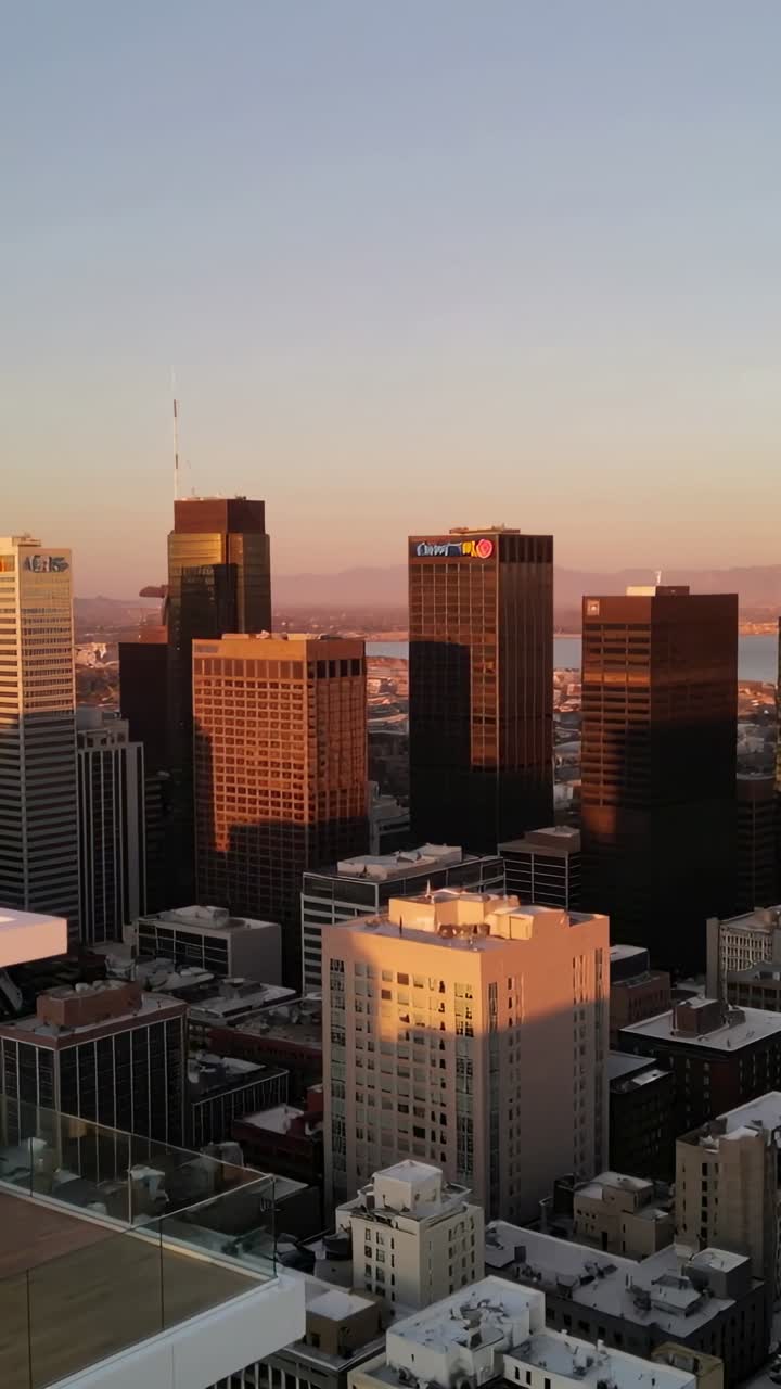 Câmera panorâmica para a direita, horizonte revelando fachadas de vidro e terraço brilhando no pôr do sol, imóveis.