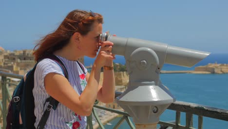 mujer mirando el paisaje marino a través de binoculares en un día soleado y ventoso