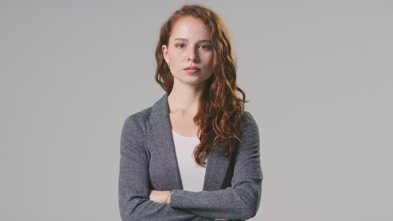 Studio Portrait Of Serious Young Businesswoman With Folded Arms Against Plain Background