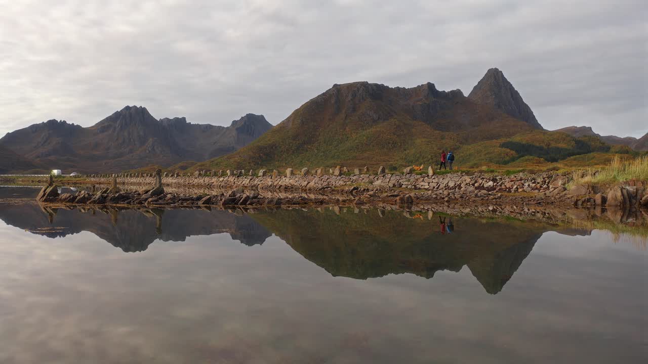 Tourists walking with a dog along Vestarelen mountain reflections in calm water
