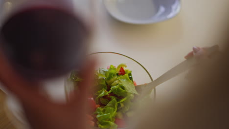 female person stirs fresh salad holding glass of red wine