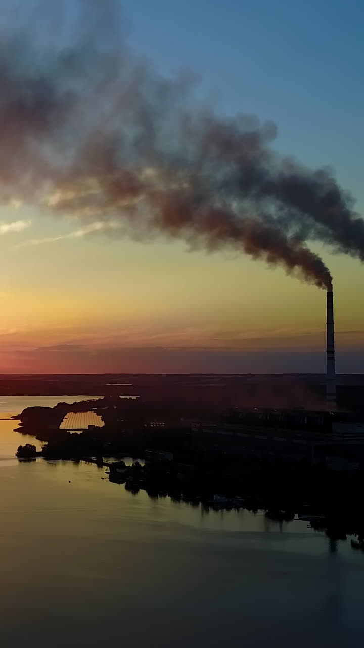 Chaminé de Fábrica Poluindo o Ar. Chaminé de fábrica poluindo o ar ao pôr do sol, problemas ambientais, fumaça das chaminés. Vídeo vertical.
