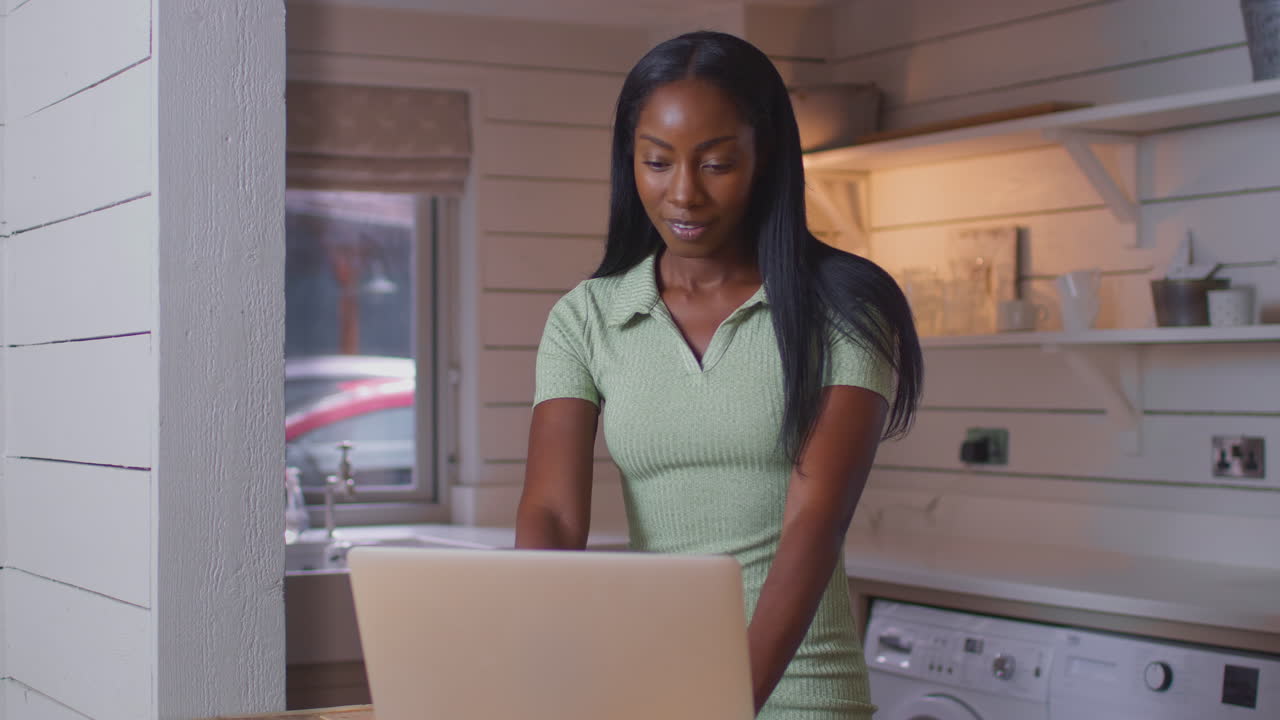 Young Woman Standing At Kitchen Counter With Laptop Working From Home