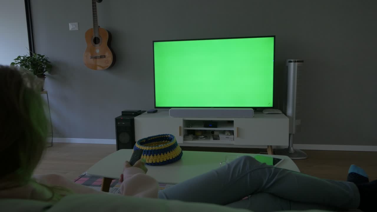 TV con schermo verde, visione a casa con il telecomando in mano.