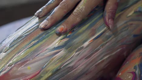 la mano de una mujer subiendo por su pierna mezclando pintura fresca y colorida sobre su cuerpo