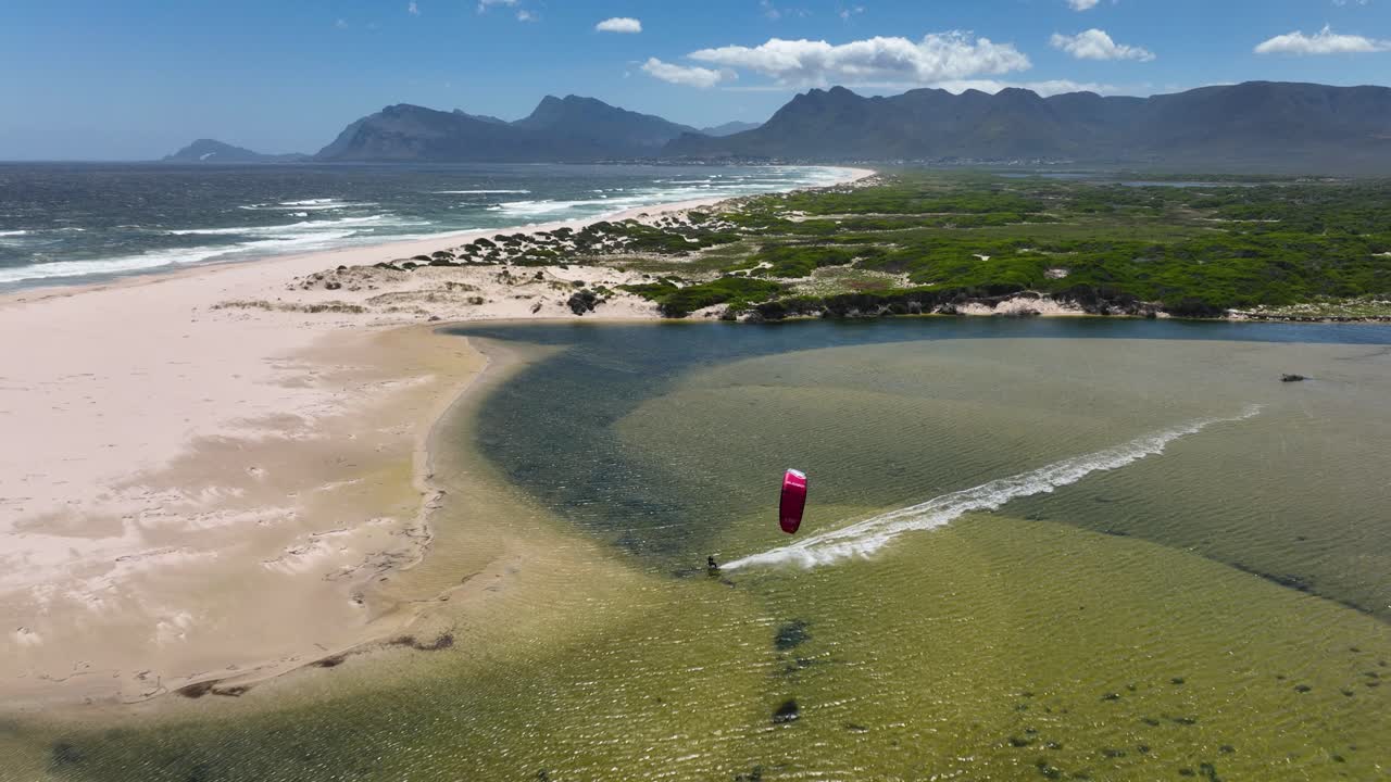 남아프리카공화국 헤르마누스 인근 배경에 장엄한 산맥이 있는 화창한 날 바다 근처 잔잔한 물에서 카이트 서퍼 경주와 스턴트를 하는 공중 와이드 샷