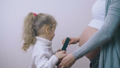 chica pone auriculares en la cintura con la madre embarazada en la pared
