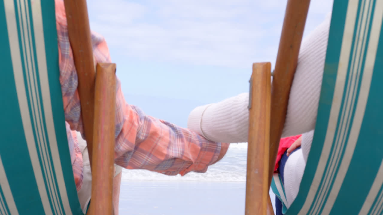 ⁇ 은 백인 노인 부부의 중간 섹션이 해변 4k에서 손을 잡고 해변에 앉아 있습니다.