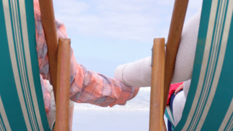 mid section of old caucasian senior couple sitting on sun lounger and holding hands at beach 4k